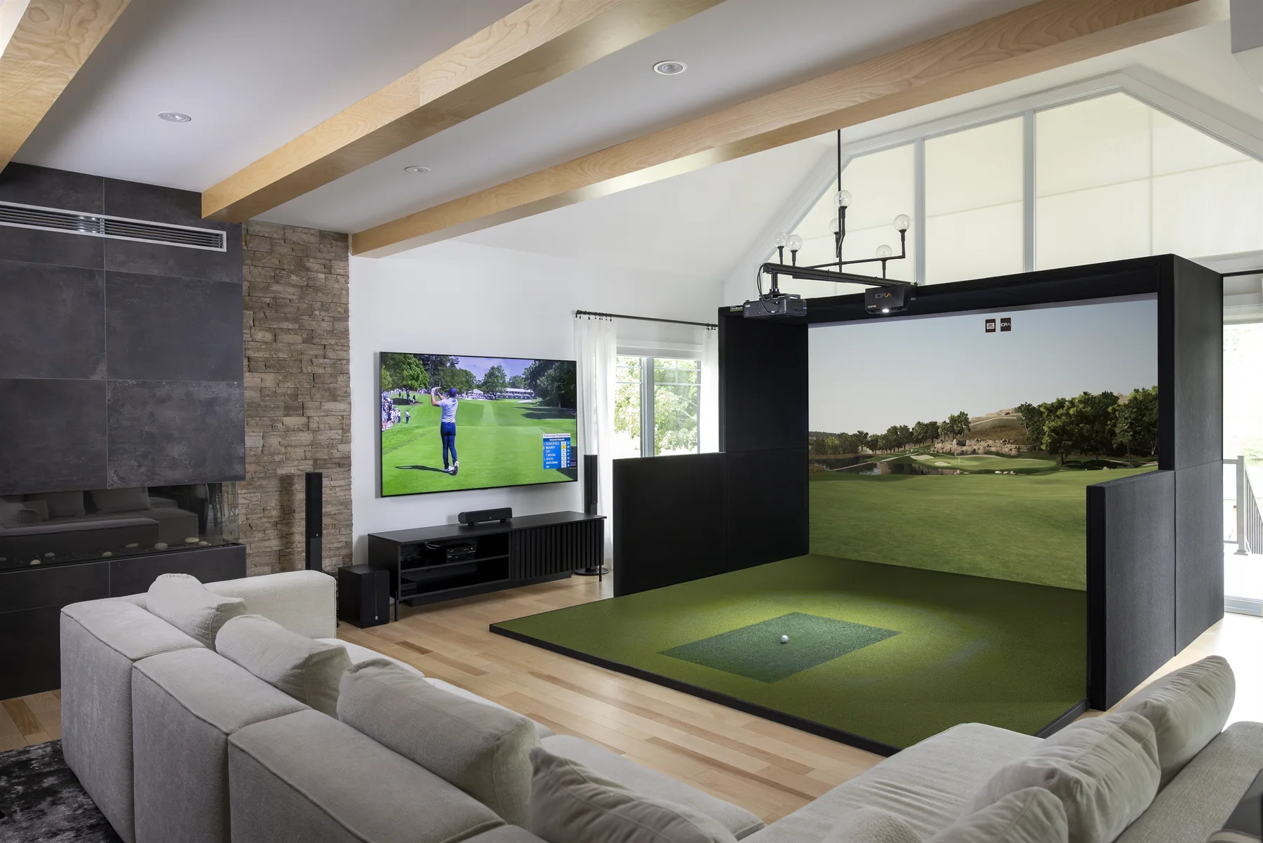 Dedicated simulator room with an impact screen, full turf surface, and comfortable lounge seating